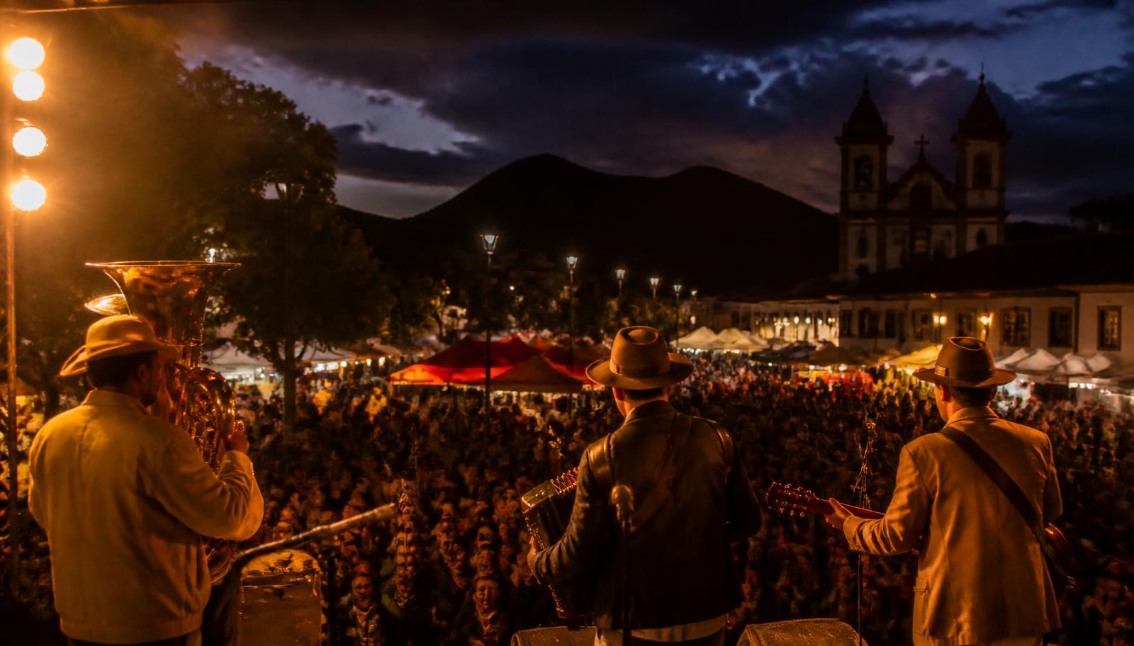 Palco de festa tradicional mineira à noite, com público e igreja colonial ao fundo